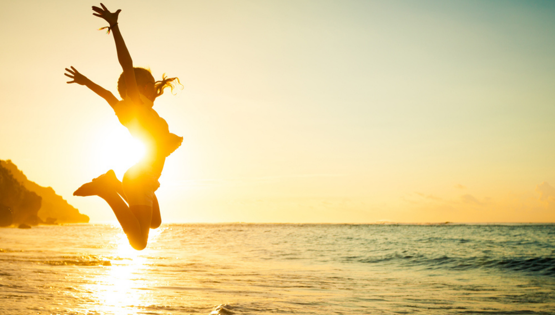 girl jumping in the air with a sunset and ocean behind her